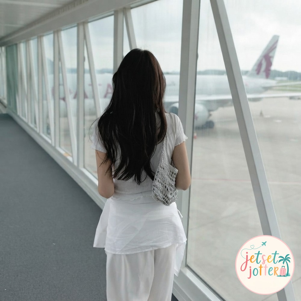 Plane selfie ideas: gazing through a jet bridge window at a parked airliner in flowing white travel wear